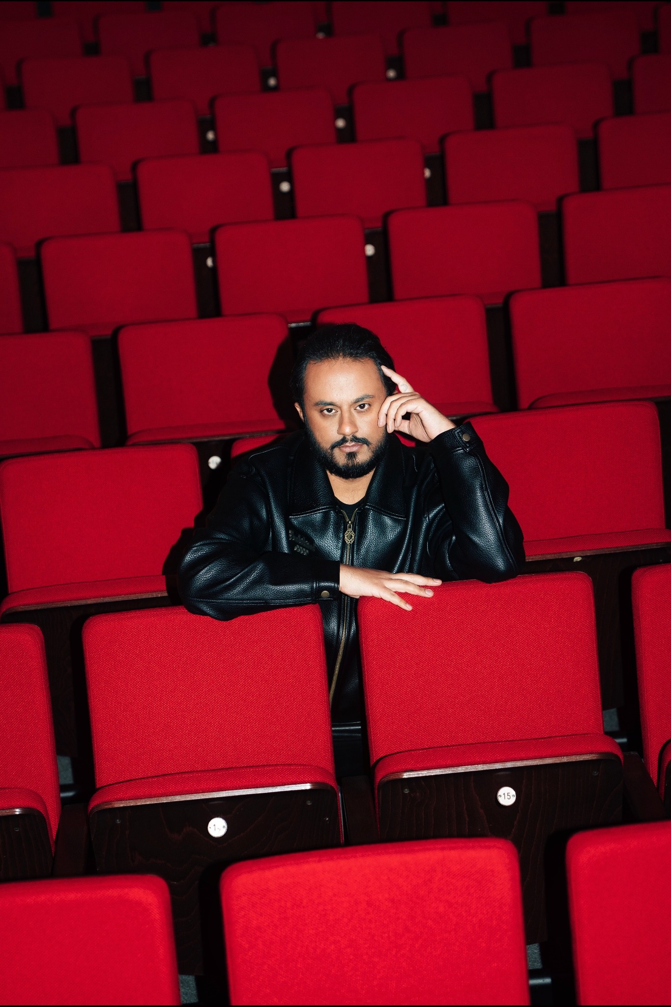 Ravi Walia zwischen roten Theaterstühlen, mit direktem Blick in die Kamera