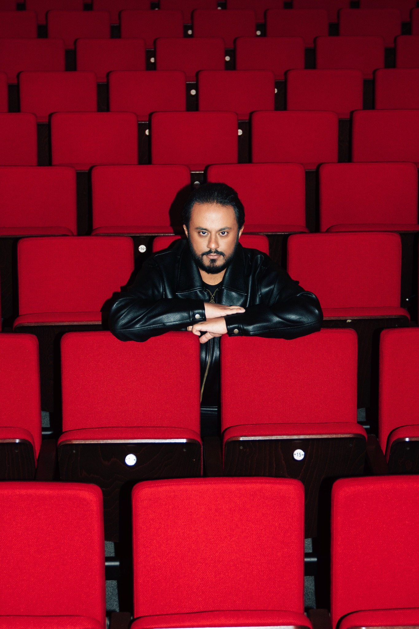 Ravi Walia in schwarzer Lederjacke zwischen roten Theaterstühlen